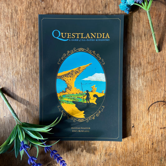 Book titled 'Questlandia' on a wooden surface with decorative faux flowers